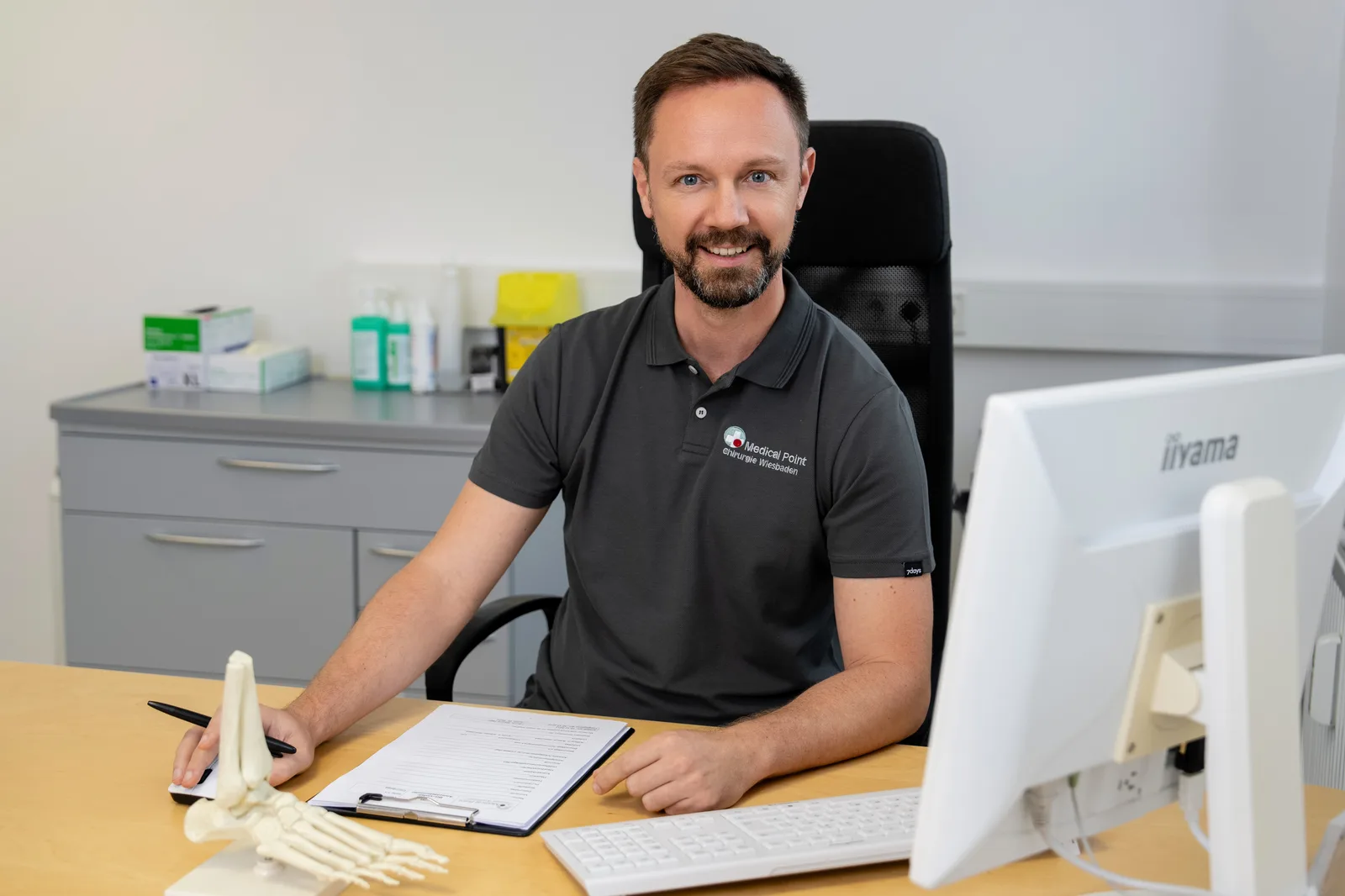 Dr. med. Michael André Müller am Arbeitsplatz mit einem Fuß- und Sprunggelenkmodell in der Praxis Medical Point Wiesbaden